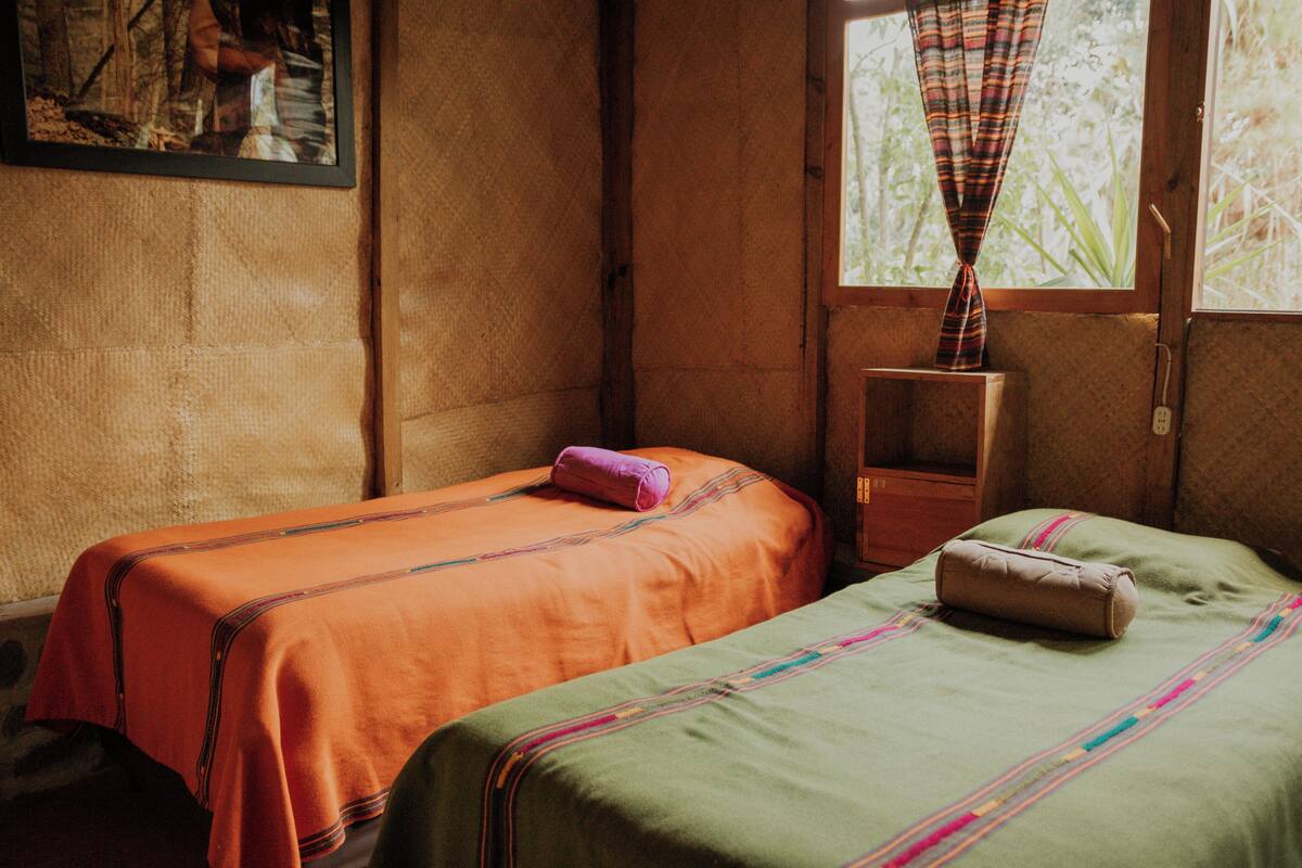 Een kamer met twee bedden, een raam met gordijnen en een houten trap.