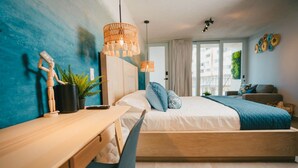 Een moderne slaapkamer met een houten bed, een bureau en een stoel. Er is een groot raam met gordijnen, een hanglamp en een kamerplant.