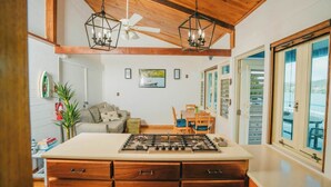 A kitchen with a central island, wooden cabinets, and a ceiling fan. There is a dining area with a table and chairs, and a view through the window. - AMAZING Ensenada Honda View @ MAREA 2-2 - Punta Aloe #3 (Culebra)