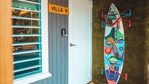 A wooden deck with a door labeled "Villa W" and a colorful surfboard hanging on the wall.