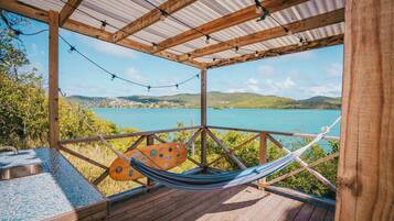 A wooden deck with a hammock and a table, overlooking a body of water and hills.