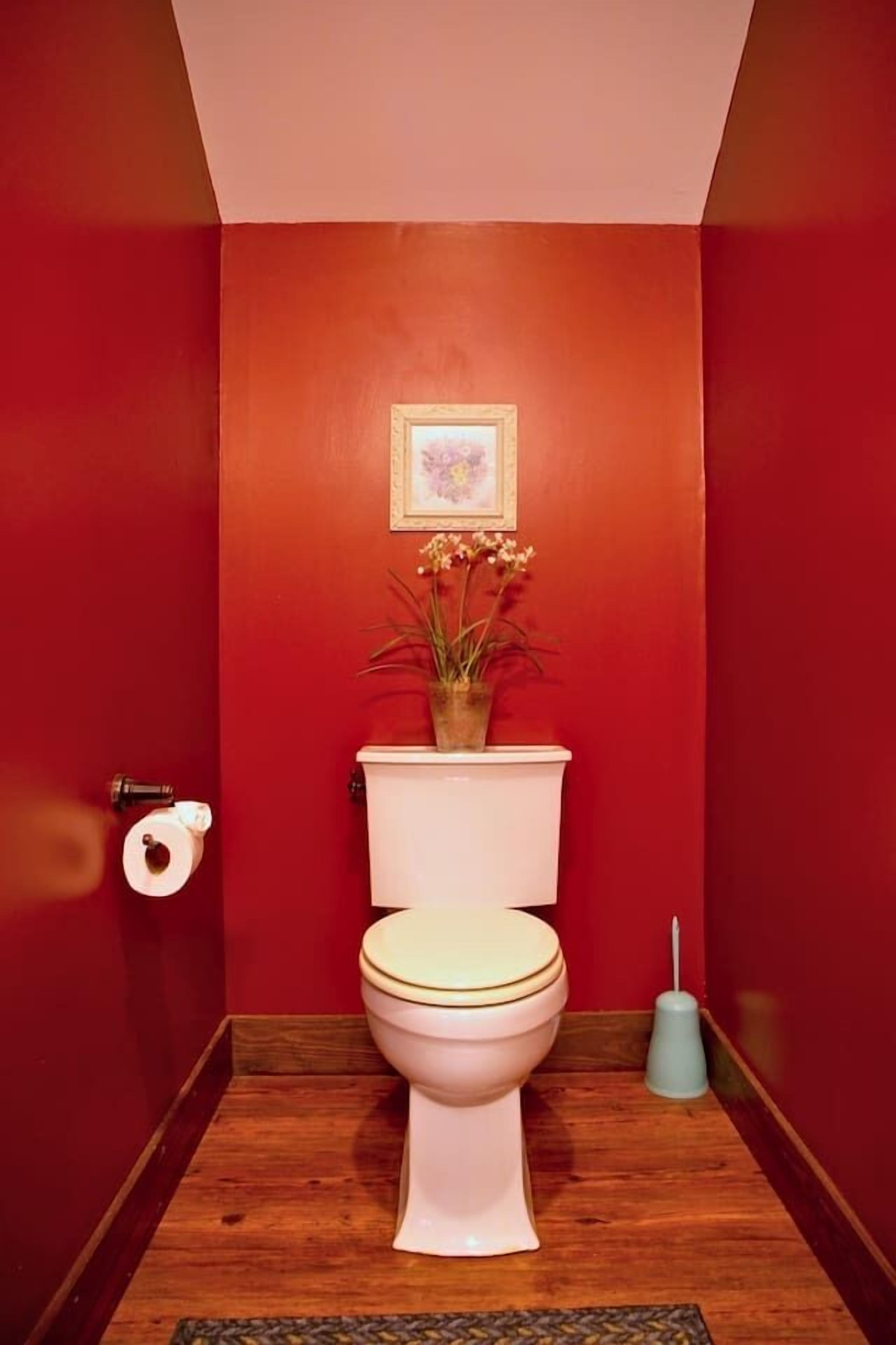 Un baño con inodoro blanco, paredes rojas y suelo de madera.