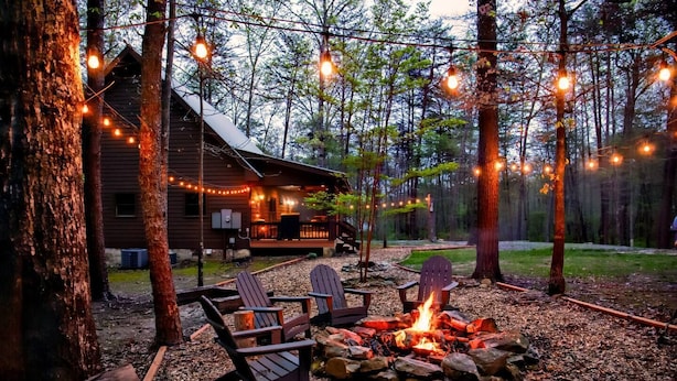 Une cabane avec un foyer et des fauteuils Adirondack, située dans un cadre forestier.