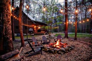 A cabin with a fire pit and Adirondack chairs in a forest setting.