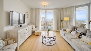 Ein modernes Wohnzimmer mit einem Flachbildfernseher, einem runden Couchtisch, einer Couch und Blick auf die Stadt durch große Fenster.