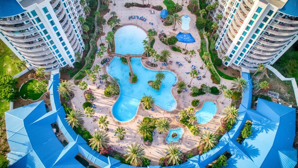 Ein Resort mit mehreren Schwimmbecken, Palmen und einer zentralen Wasserrutsche.