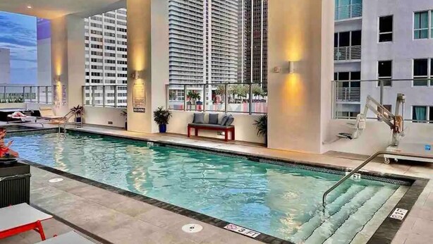 Une piscine avec un espace de détente, entourée d’immeubles de grande hauteur.