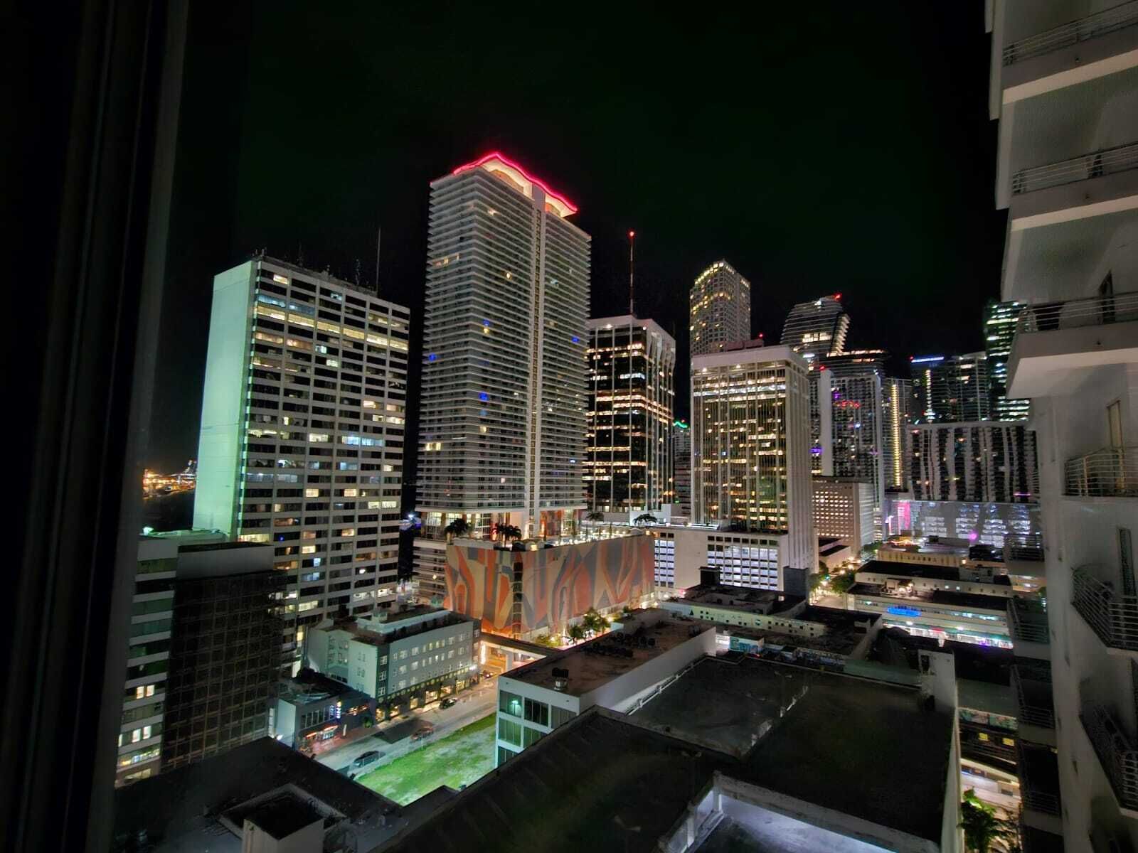 A high-rise urban area with multiple buildings, some with illuminated windows and one with a red-lit top.