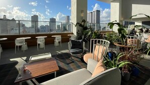 Un salon moderne situé sur le toit, avec des sièges, des plantes et une vue sur la ville.