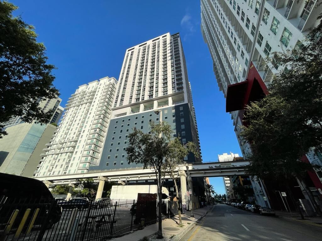 Ein Hochhaus mit mehreren Stockwerken und Balkonen, umgeben von Bäumen und blauem Himmel.