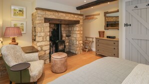 A cozy room with a stone fireplace, a green armchair, a wooden bench, and a dresser with a mirror. - Kyte Cottage (Shipston on Stour)