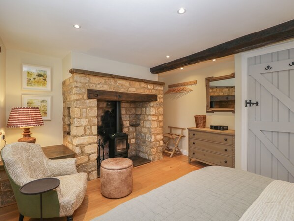 A cozy room with a stone fireplace, a green armchair, a wooden bench, and a dresser with a mirror. - Kyte Cottage (Shipston on Stour)
