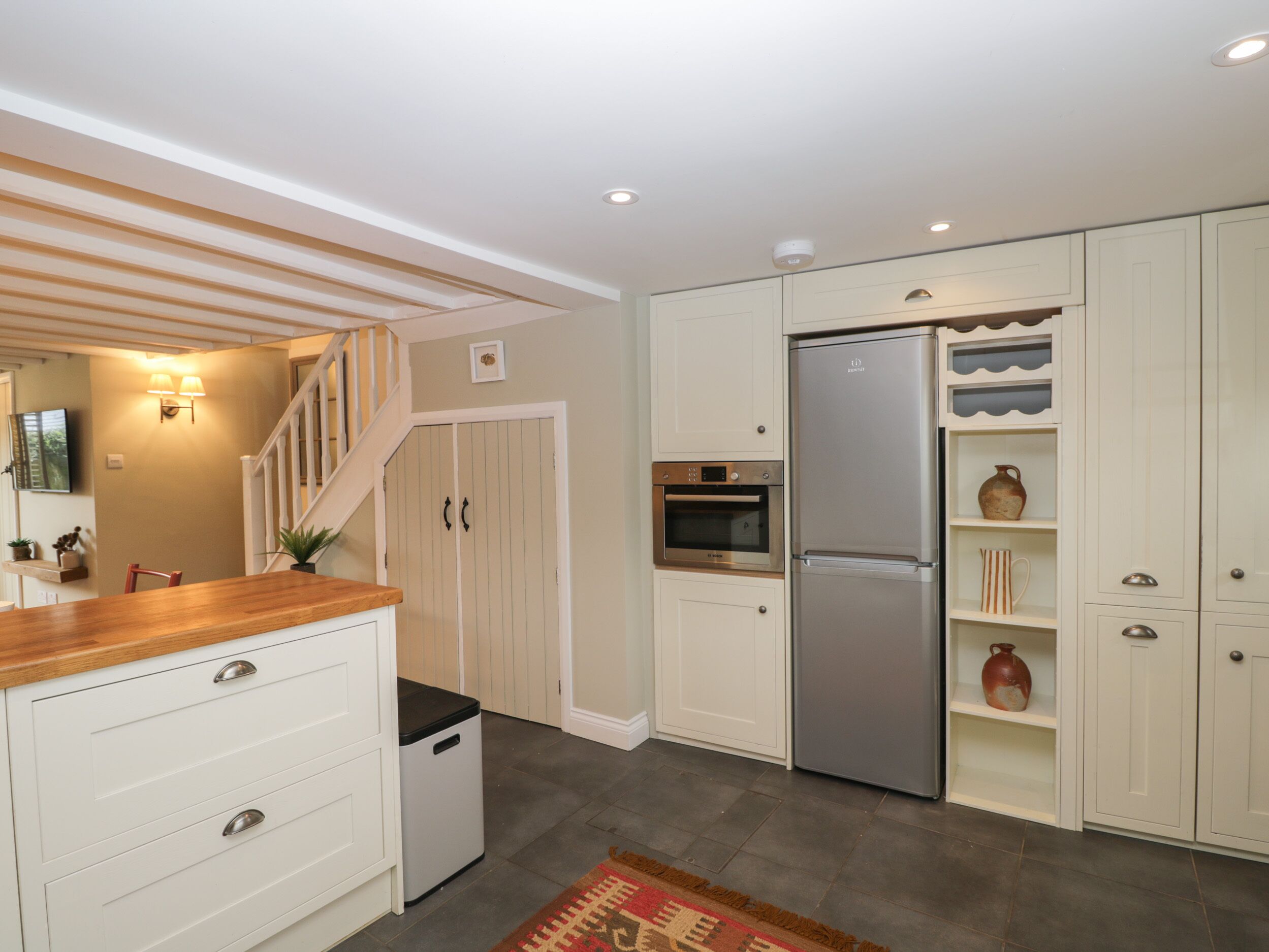 A modern kitchen with white cabinetry, a stainless steel refrigerator, an oven, and a microwave. There is a wooden countertop and a small trash bin.