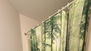 Un bagno con tenda da doccia a tema foresta, un portasciugamani con un asciugamano bianco e pavimento piastrellato.