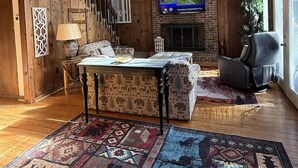 Een ruime loft met zichtbare houten balken, een open haard, een televisie en een groot vloerkleed.