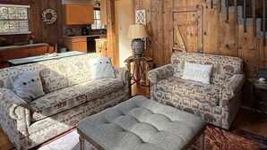 Een rustiek cabin interieur met slaapkamer op een entresol, houten wanden, een trap en een gezellige woonruimte met gestreept meubilair.