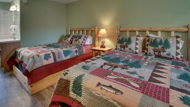 A room with two beds, each with a distinct quilt featuring animal and nature patterns. - Bavarian Brook 7A (Helen)