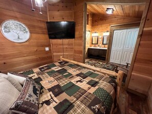 A wooden cabin bedroom with a large bed, a mounted TV, and a mirror above the dresser. - Bavarian Hideaway 25 (Sautee Nacoochee)