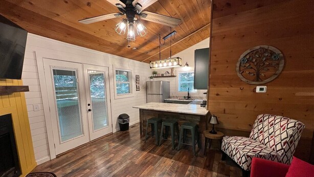 A cozy cabin interior with a wooden ceiling, a fireplace, a dining area with stools, and a patterned armchair. - Bavarian Hideaway 25 (Sautee Nacoochee)