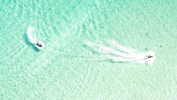 Duidelijk uitzicht op een strand met twee boten die rimpelingen in het water veroorzaken.