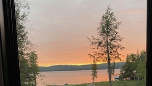 Een laptop op een bureau met uitzicht op een meer en bomen bij zonsondergang.