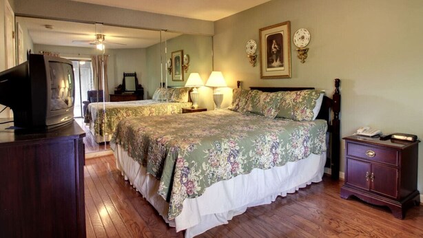 A bedroom with two beds, a wooden dresser, a nightstand, a ceiling fan, and a television. - Rivers Edge 504 (Helen)