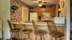A kitchen with wooden cabinets, a central island with stools, a ceiling fan, and a refrigerator. - Rivers Edge 504 (Helen)