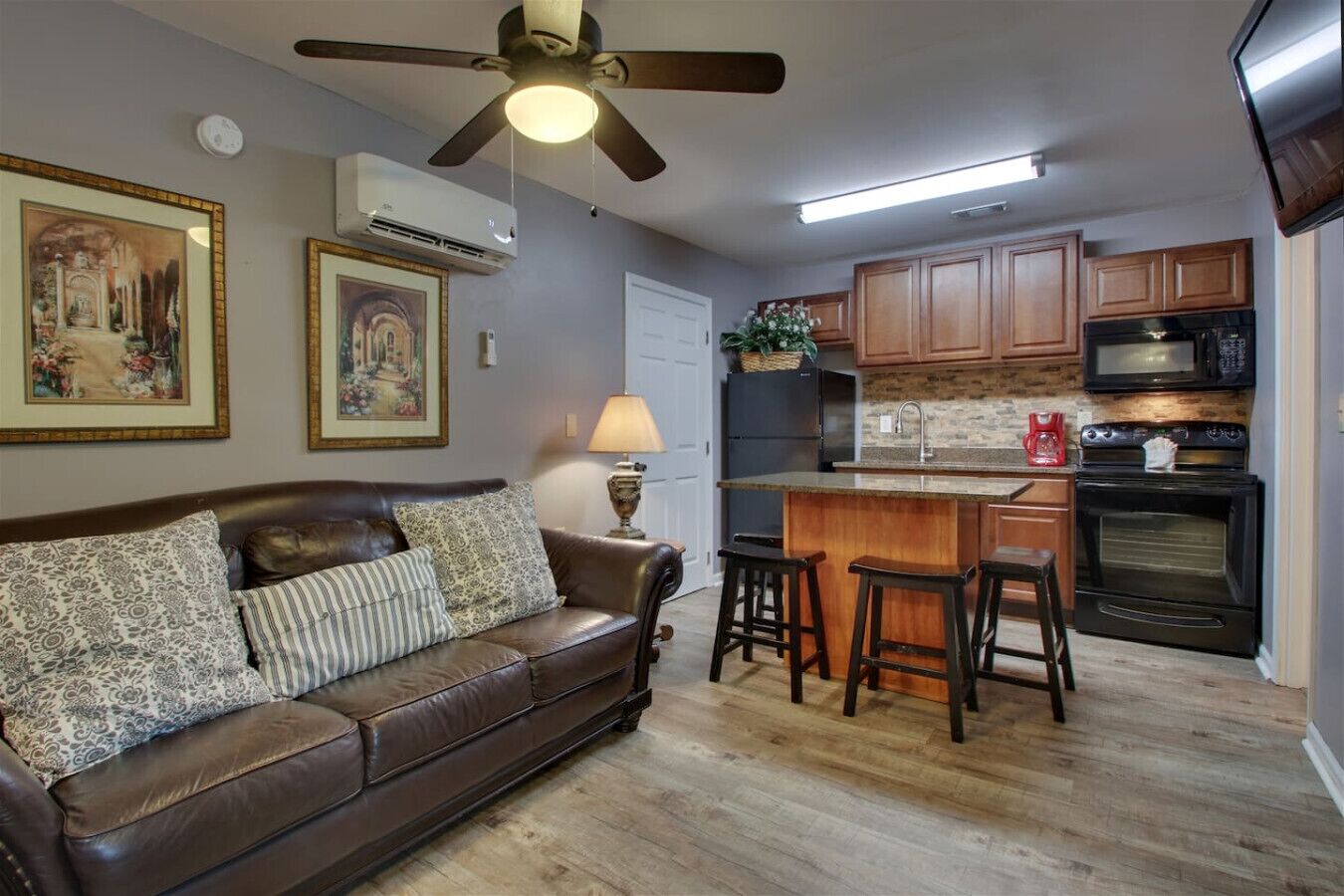 A cozy living room with a brown leather couch, a ceiling fan, and two framed paintings on the wall.