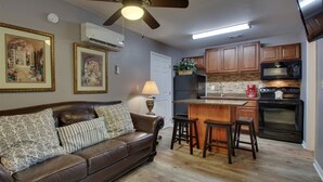 Un salon chaleureux avec un canapé en cuir marron, un ventilateur de plafond et deux tableaux encadrés accrochés au mur.