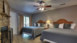 Une chambre d’hôtel avec deux lits, un ventilateur de plafond, une lampe et une cheminée en pierre.