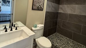 Un baño con lavamanos blanco, inodoro y zona de ducha con azulejos oscuros.