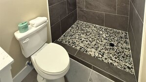 Un baño con ducha, paredes de azulejos, un inodoro y un cuadro en la pared.