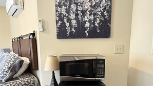 Un dormitorio con cama, mesita de noche, lámpara, microondas y refrigerador.