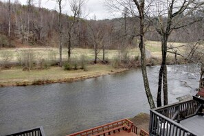 A riverside view from a deck with a railing, overlooking a river and a forested area. - Rivers Edge Condo 902 (Helen)