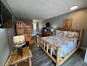 A bedroom with a wooden bed, a nightstand, a lamp, a TV, and a staircase. - Bavarian Brook Unit 4a (Helen)