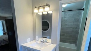 A bathroom with a white vanity, a round mirror, and a shower area. - Bavarian Brook Unit 8 (Helen)
