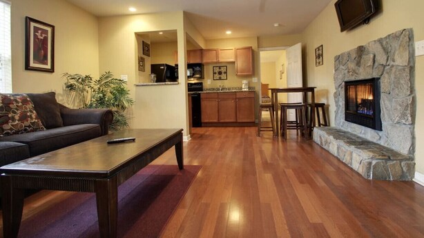 Un salon avec une cheminée, un plancher en bois, un canapé, une table basse et, au fond, un coin cuisine.