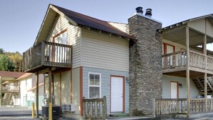 Un bâtiment à deux étages, doté d’une cheminée en pierre, d’un balcon avec une balustrade en bois et d’une porte blanche.
