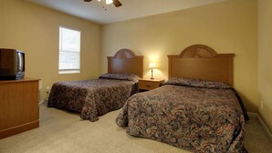 Une chambre avec deux lits, un ventilateur de plafond, une table de chevet avec une lampe et un téléviseur posé sur une commode.