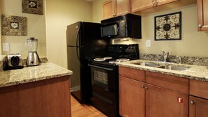 Une cuisine avec des meubles de rangement en bois, un réfrigérateur noir, un four à micro-ondes, une cuisinière et un plan de travail en granit.