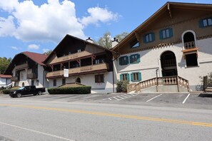 A hotel with a traditional architectural style, featuring balconies, a parking lot, and a clear sky.