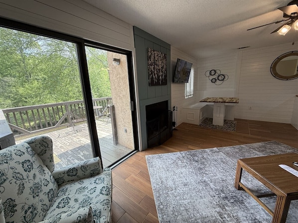 A cozy living room with a fireplace, a sofa, a coffee table, and a balcony with a wooden deck. - Rivers Edge 802 (Helen)