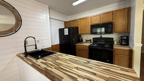 A kitchen with a wooden countertop, black appliances, and wooden cabinets. - Rivers Edge 802 (Helen)