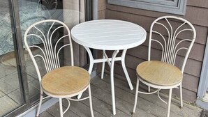 A small outdoor seating area with a round table and two chairs, a glass door, and a window with blinds. - Rivers Edge 803 (Helen)