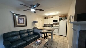 A compact living space with a black leather sofa, a small coffee table, a ceiling fan, a kitchen area with white cabinets, and a fireplace. - Rivers Edge 803 (Helen)