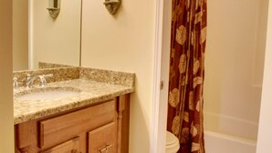 A bathroom with a granite countertop sink, wooden cabinets, a toilet, and a shower curtain with a leaf pattern. - Bavarian Brook Condo 15 (Helen)