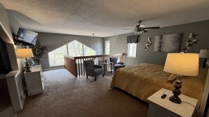Een slaapkamer met een bed, bedlampen, een bureau, een stoel, een televisie en een balkon.