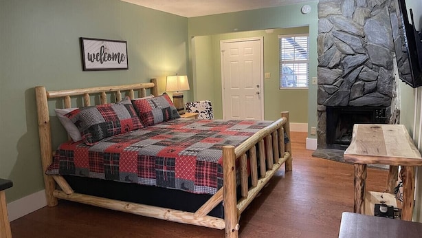 A bedroom with a wooden bed, a stone fireplace, and a welcome sign. - Bavarian Brook Unit 7 (Helen)