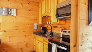 A wooden cabin kitchen with wooden cabinets, a granite countertop, a coffee maker, a stove, and a microwave. - Bavarian Hideaway 24 (Sautee Nacoochee)
