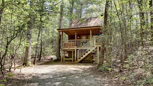 A cabin with a wooden deck and stairs leading to a balcony, surrounded by a forest. - Bavarian Hideaway 24 (Sautee Nacoochee)